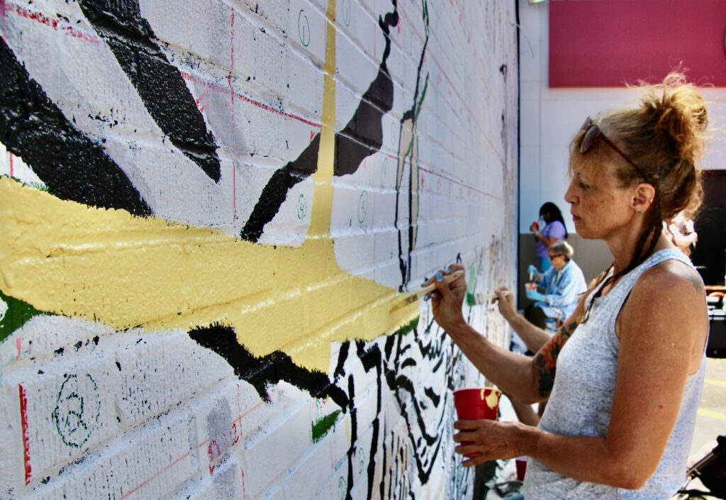(Rick Miller/Olean Star) Rolita Wielkie paints a yellow portion of the Olean mural “The Moment,” designed by Alex Derwick.”