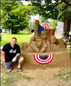 (Eric Jones Photo) West Clarksville sculptor Eric Jones kneels beside a sand sculpture he made at the Allegany County Fair of former President Donald Trump pumping his hand in the air after an assassination attempt at a political rally in Butler, Pa., last week.