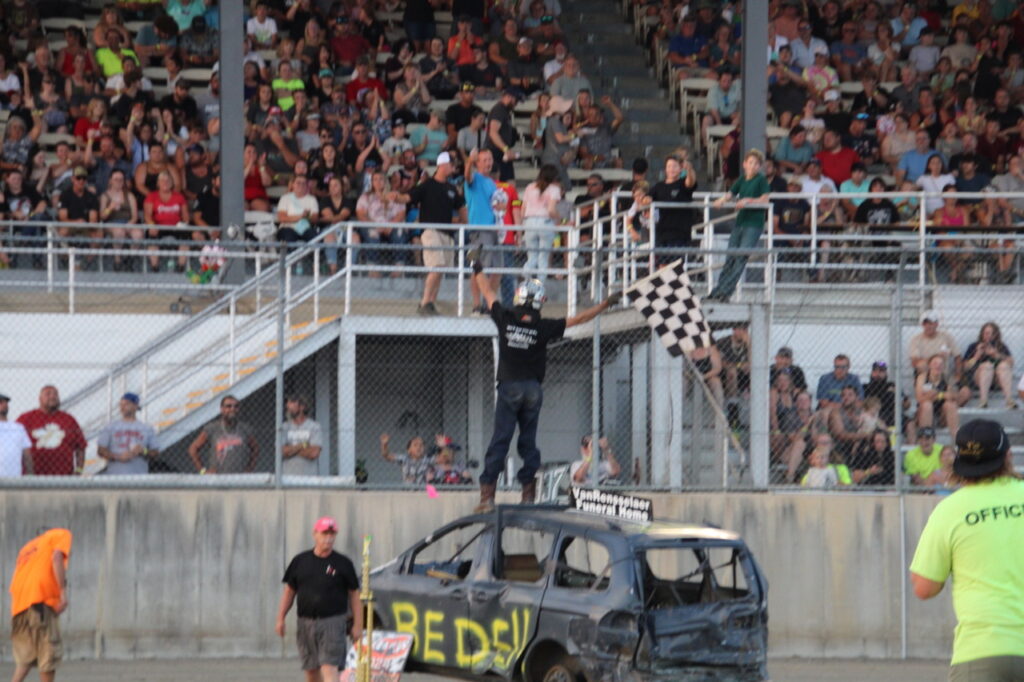 (Rick Miller/Olean Star)
Craig Bedell of Little Valley waves the checkered flag from the roof of his minivan after winning heat 2 at the demolition derby at the 181st Cattaraugus County Fair Monday. The second demolition derby is Saturday night.