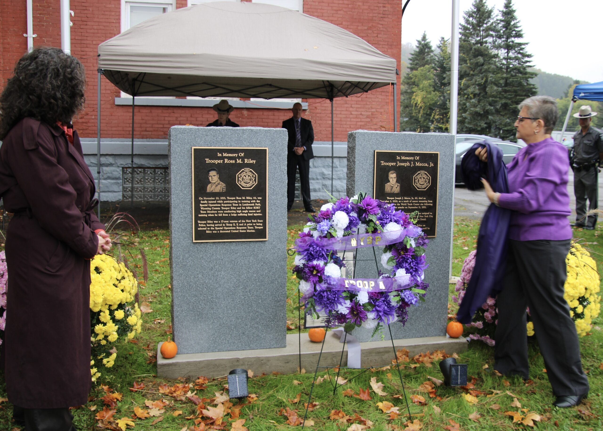 (Rick Miller/Olean Star) Linda Mecca (right) removes a cover from the memorial for her husband Trooper Joseph J. Mecca Jr., is a memorial dedication ceremony Sunday in front of the Olean State Police Substation on Homer Street in Olean. Retired Sgt. Heidi Riley had just unveiled a memorial to her late husband Trooper Ross M. Riley. Both troopers' deaths were in the line of duty.