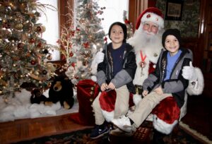 (Rick Miller/Olean Star) Twins Khalib Burney (left) and Khalil, sons of Malik Burney of Olean, sit on Santa’s lap Saturday at the Victorian Christmas celebration at the Fannie Bartlett House.