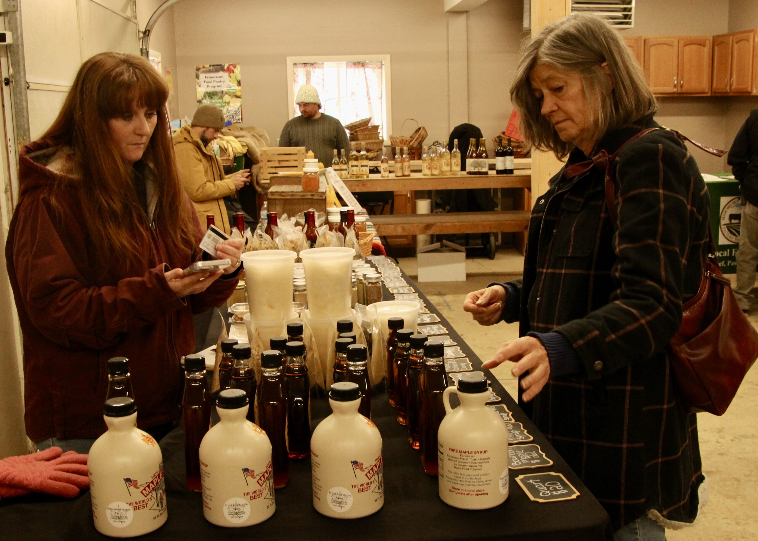 (Rick Miller/Olean Star) Kellie Bernd (left) of Brookside Maple in Centerville, waits on a shopper Saturday at the Olean Farmers Market that will set up at Canticle Farm Market on Old State Road in Allegany every other Saturday from 11 a.m. to 2 p.m. for the next two months.
