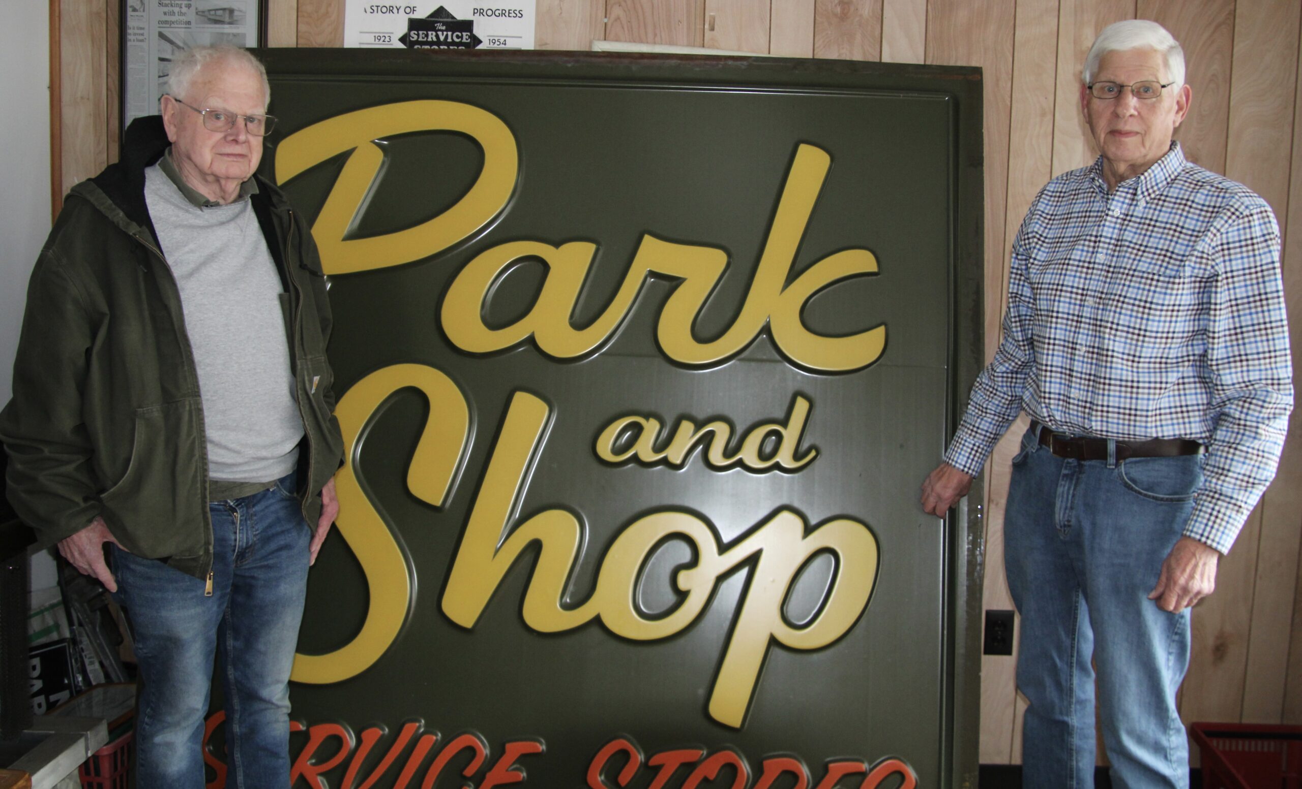 (Rick Miller/Olean Star) Paul Mahar (left) and his brother Tom stand beside a Park and Shop sign that once hung on its former West State Street store in Olean. They and their brother Jim have decided to retire. They lease the remaining Park and Shop store on Front Street in Olean to Jim Mahar’s son, Jim Mahar Jr.
